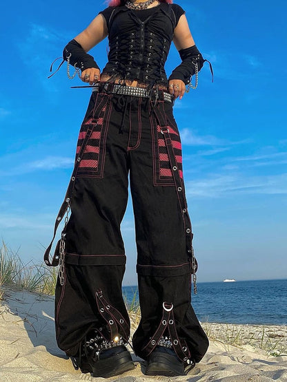 Frau in schwarzer Gothic-Hose mit pinken Streifen am Strand, alternative Mode.