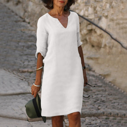 Frau in weißem Leinenkleid, V-Ausschnitt, Sommermode, eleganter Stil, Kopfsteinpflasterweg.
