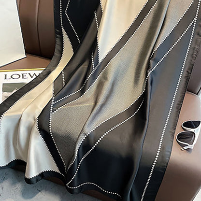 Schwarzer und beiger Seidenschal mit geometrischem Muster auf Ledersofa.
