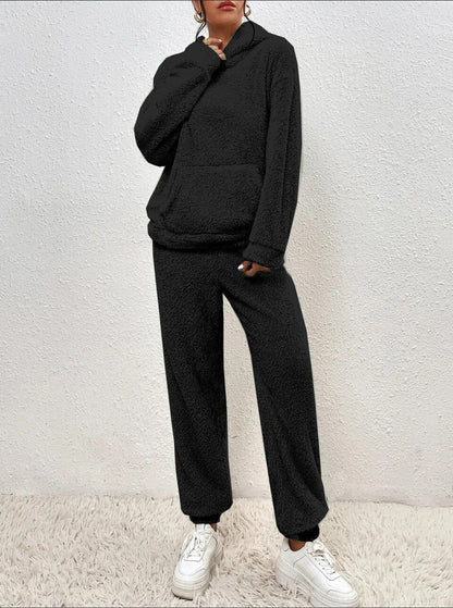Frau in schwarzem Fleece-Hoodie und Jogginghose, weiße Sneaker, gemütliche Wintermode.