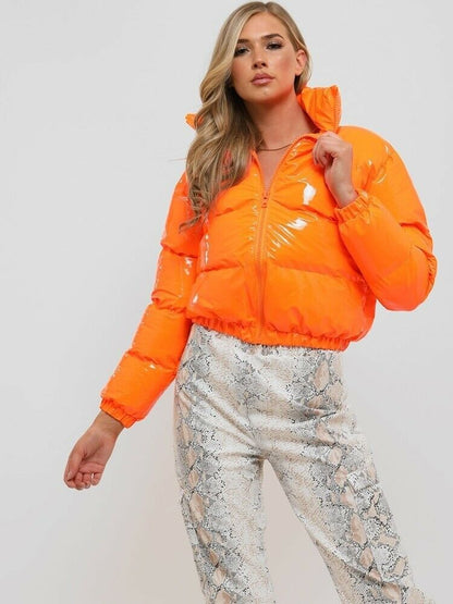 Frau in leuchtend orange glänzender Daunenjacke und Schlangenlederhose, modisch, auffällig.