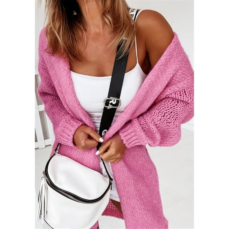 Frau in rosa Strickjacke mit weißem Top und weißer Umhängetasche, modisch, lässig.