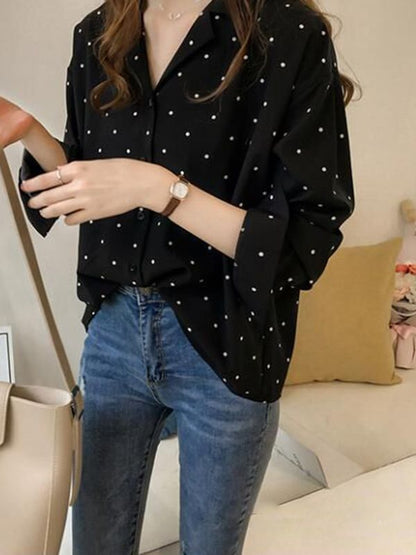 Frau in schwarzer gepunkteter Bluse, blaue Jeans, beige Tasche, Armbanduhr, modisch, lässig.