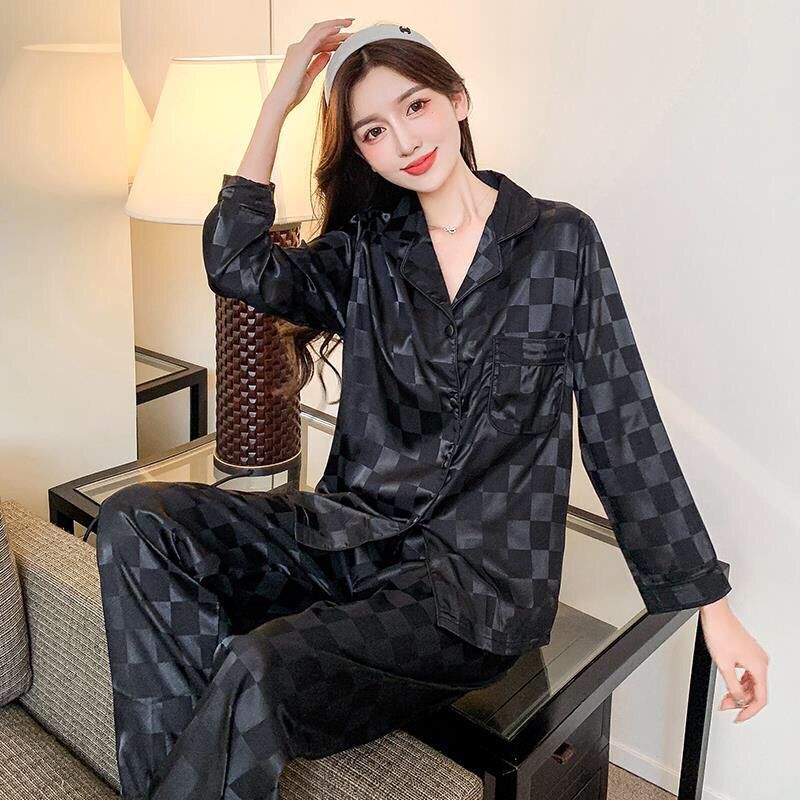 Frau in schwarzem Satin-Pyjama mit Karomuster sitzt auf Sofa, stilvolle Nachtwäsche.