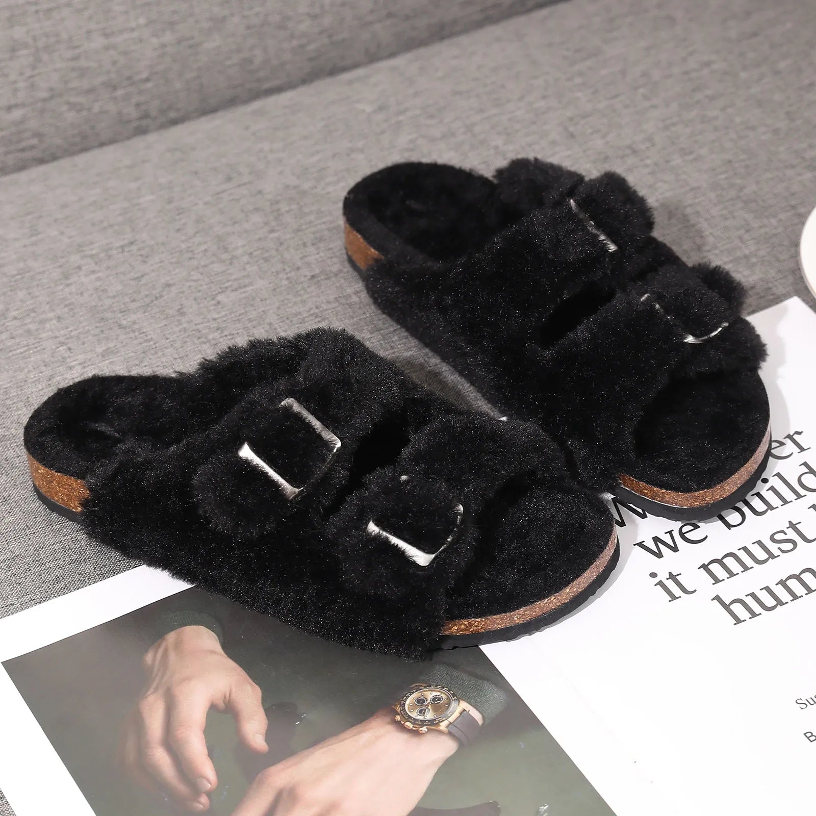 Schwarze Fell-Pantoffeln mit Schnallen auf grauem Hintergrund, gemütliche Hausschuhe Damen.