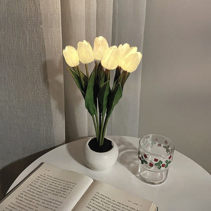 Künstliche Tulpen im weißen Keramiktopf auf Tisch, neben Buch und Glas, moderne Dekoration.
