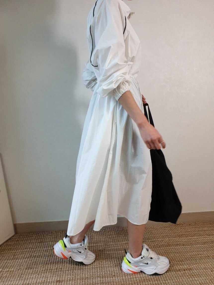 Frau in weißem Kleid mit Sneakers und schwarzer Tasche, seitliche Ansicht, moderne Mode.