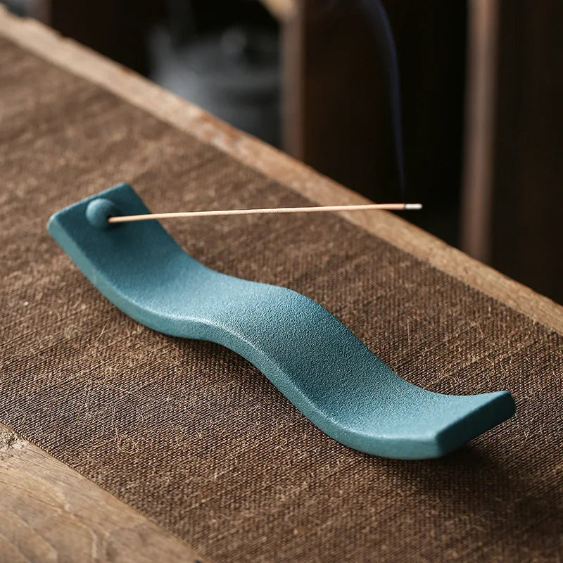 Grüner Keramik-Räucherstäbchenhalter auf Holztisch, wellenförmig, modern, dekorativ.