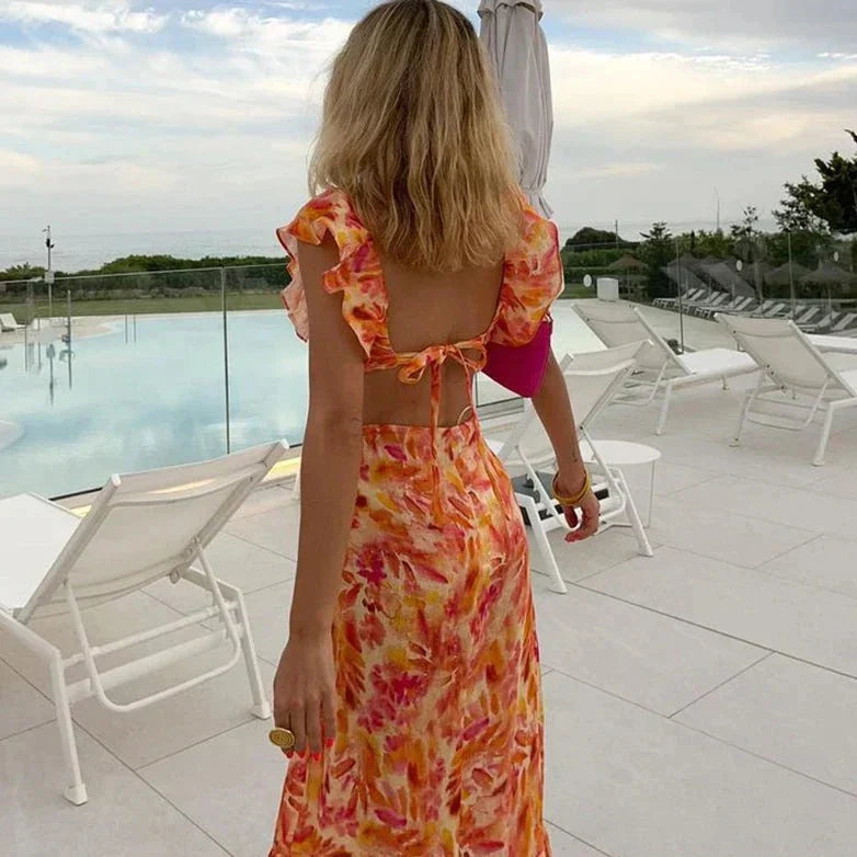 Frau im Sommerkleid mit Blumenmuster am Pool, Rückenansicht, entspannte Urlaubsatmosphäre.