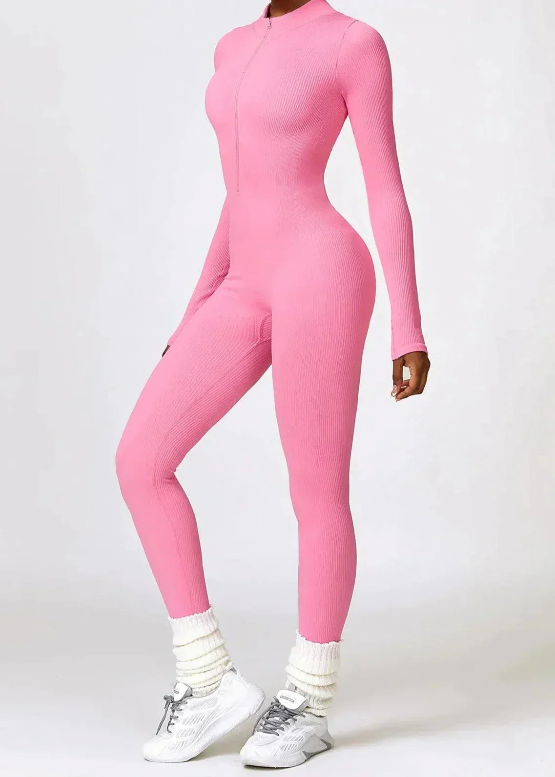 Frau in rosa, nahtlosem Jumpsuit, langärmelig, figurbetont, mit weißen Sneakers.