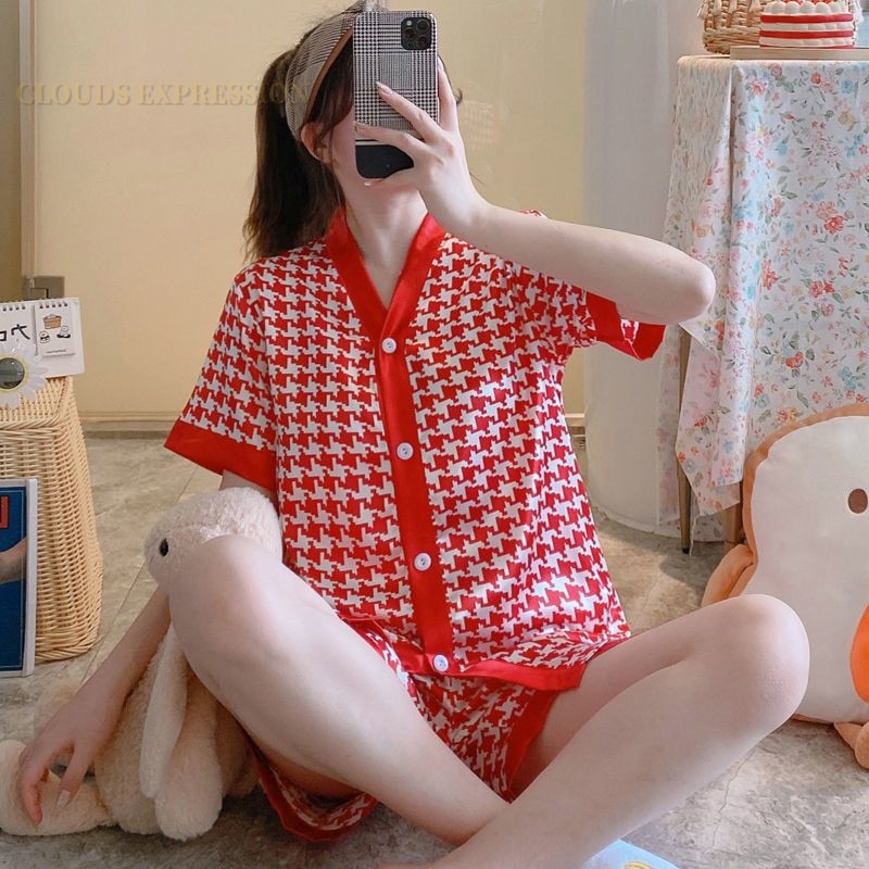 Frau in rotem Pyjama mit Hahnentrittmuster, sitzt auf Boden, Selfie mit Smartphone.