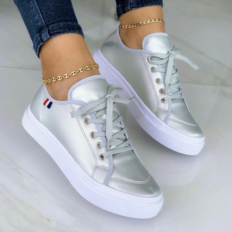 Silberne Damen-Sneaker mit weißer Sohle, Schnürsenkeln und goldener Fußkette.