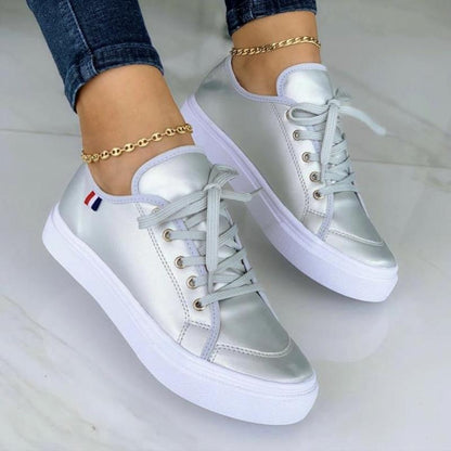Silberne Damen-Sneaker mit weißer Sohle, Schnürsenkeln und goldener Fußkette.