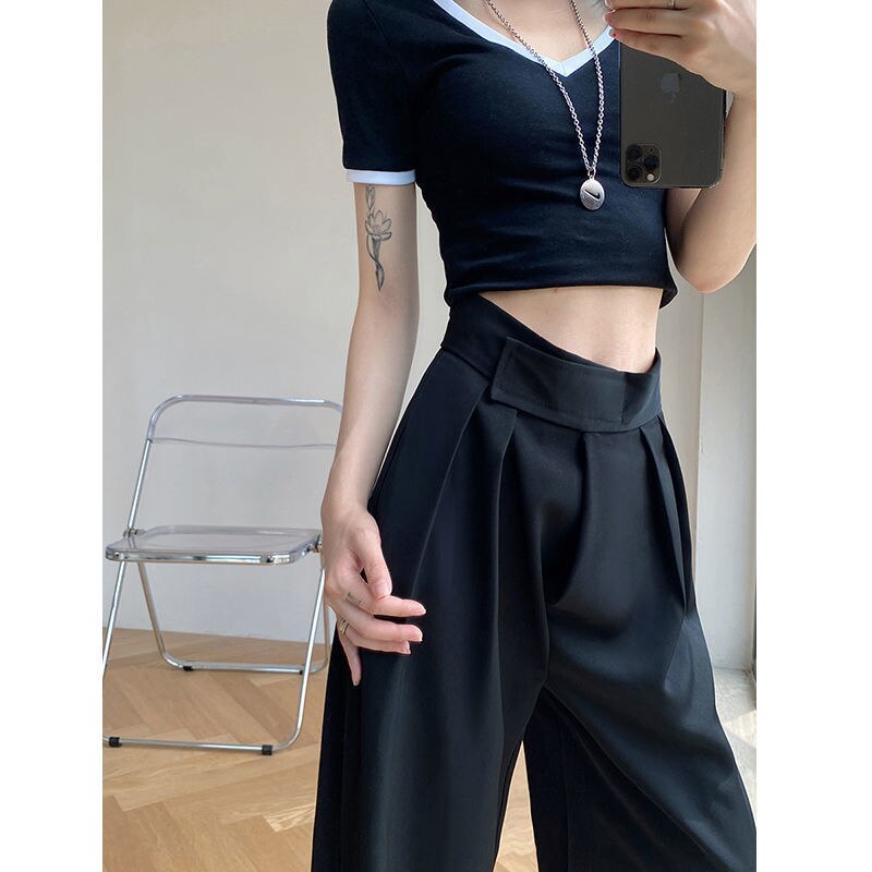 Frau in schwarzem Crop-Top und weiten Hosen, moderner Stil, Innenraum, Smartphone in Hand.