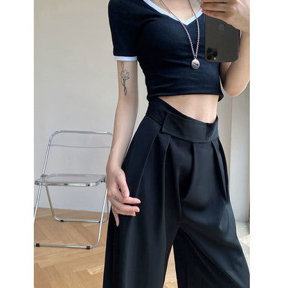 Frau in schwarzem Crop-Top und weiten Hosen, moderner Stil, Innenraum, Smartphone in Hand.