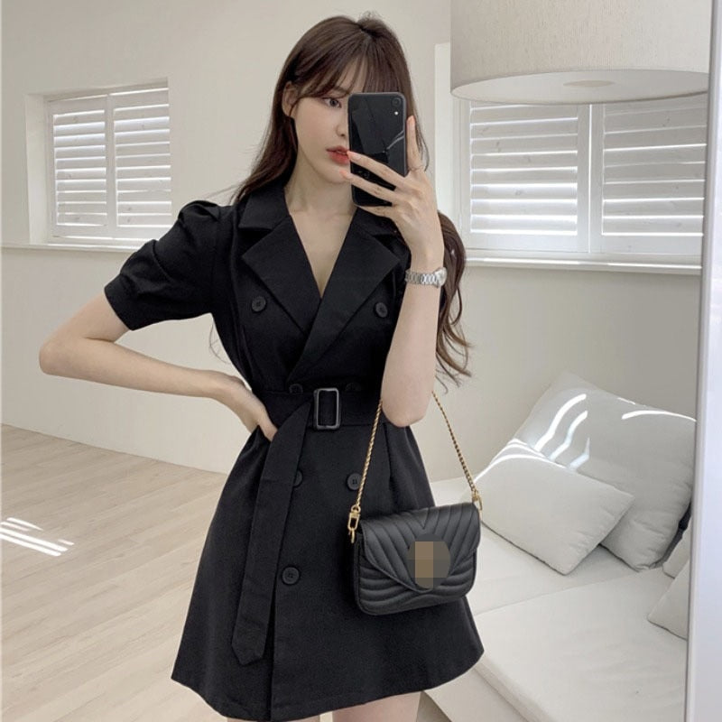 Frau in schwarzem Trenchcoat-Kleid mit schwarzer Umhängetasche, modernes Wohnzimmer.