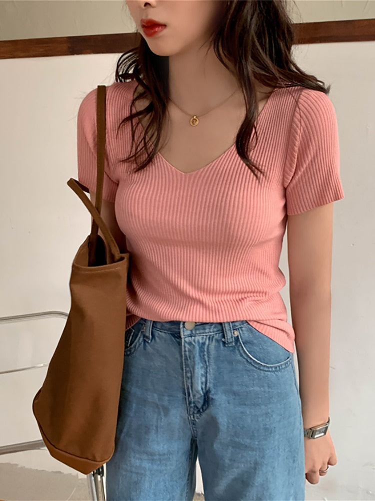 Frau in rosa geripptem T-Shirt, blaue Jeans, braune Tasche, lässiger Stil.