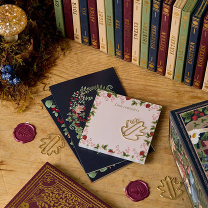 Notizbücher mit floralen Mustern auf Holztisch, umgeben von bunten Büchern und Wachssiegeln.