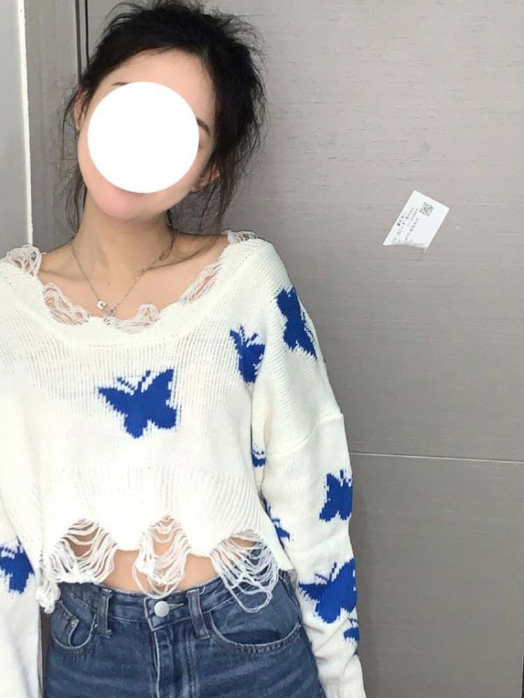 Frau in weißem Strickpullover mit blauen Schmetterlingen, zerrissener Saum, modisch, lässig.