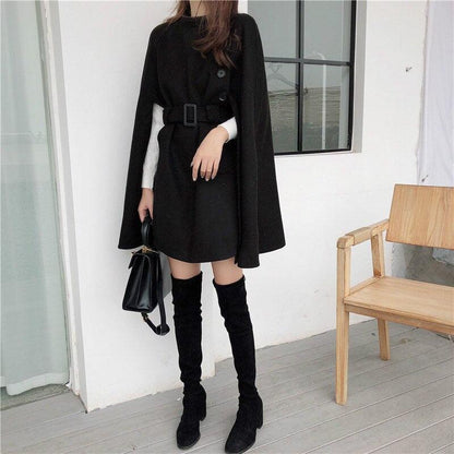 Frau in schwarzem Cape-Kleid mit Gürtel, Overknee-Stiefeln, Handtasche, moderne Mode.