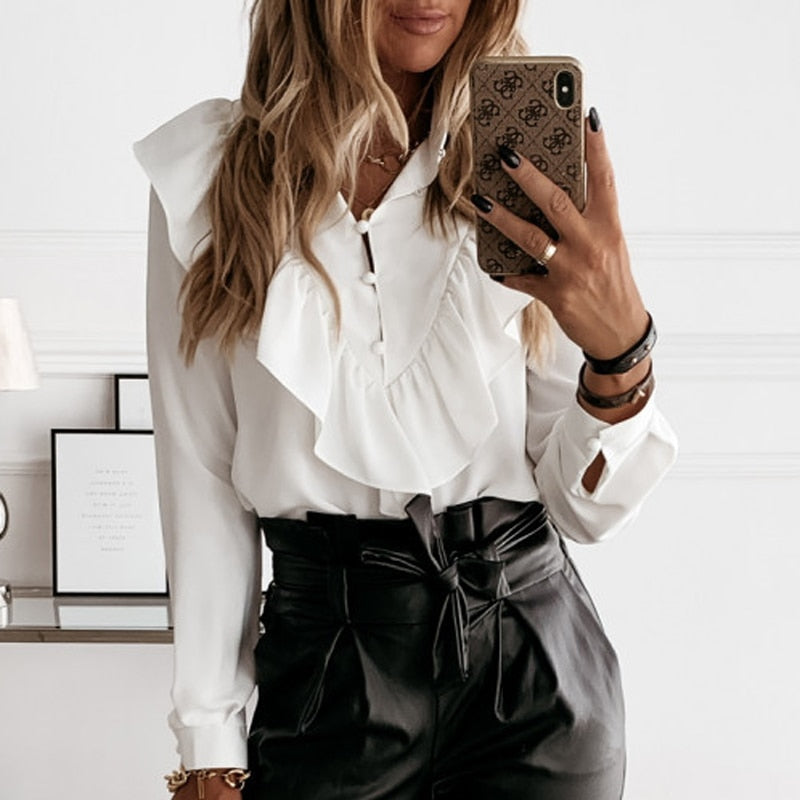 Frau in weißer Rüschenbluse und schwarzer Lederhose, hält Smartphone, modisches Outfit.