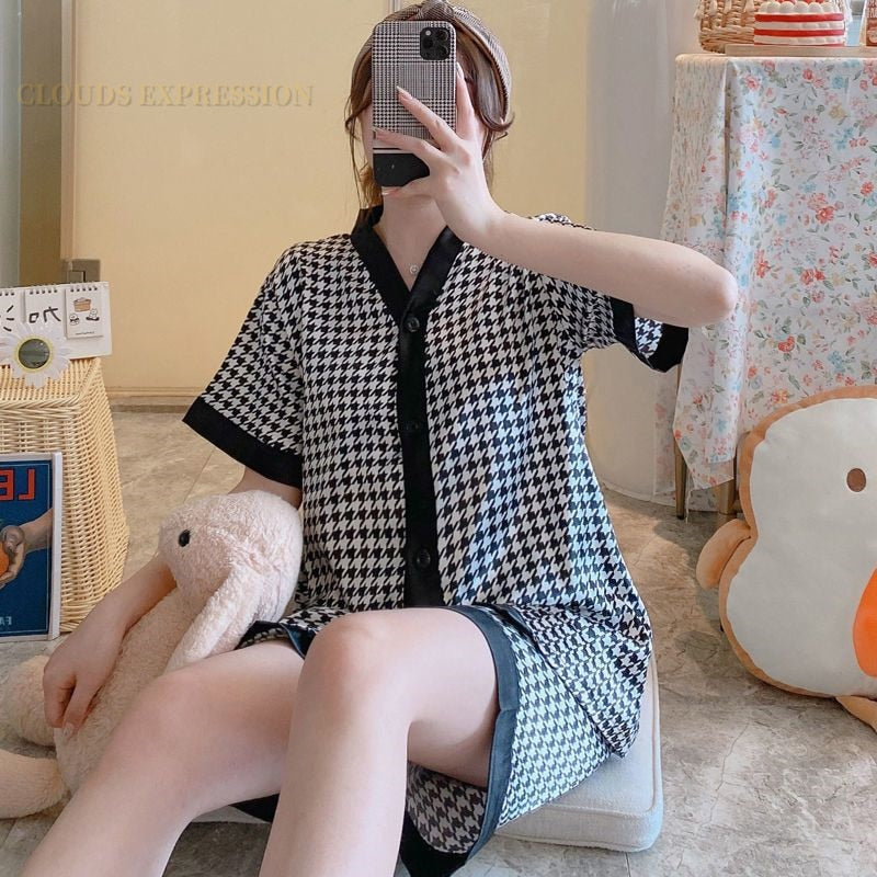 Frau in schwarz-weißem Hahnentritt-Pyjama, sitzt mit Plüschtier, modernes Schlafzimmer.
