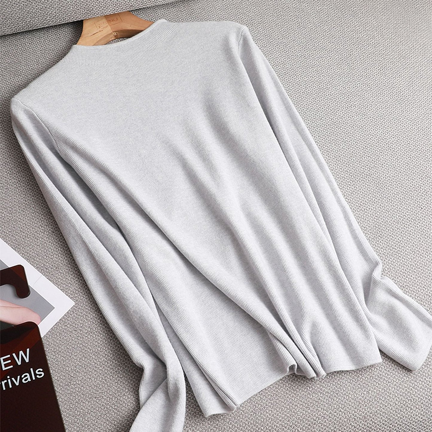 Grauer Damenpullover aus Baumwolle, langärmelig, elegant, auf Kleiderbügel, Herbstmode.