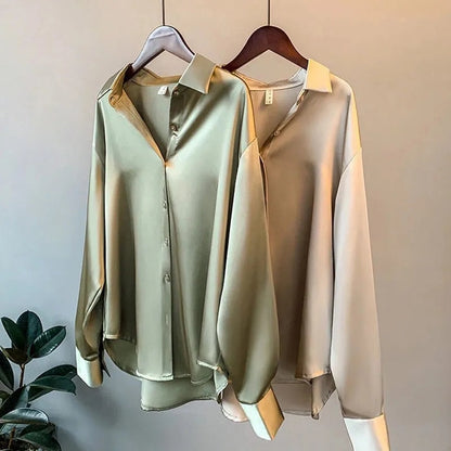 Zwei seidene Blusen in Grün und Beige auf Kleiderbügeln, elegante Damenmode, langärmlig.