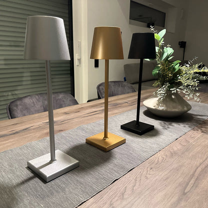 Drei moderne Tischlampen in Silber, Gold und Schwarz auf Holztisch, minimalistisch, LED-Beleuchtung.