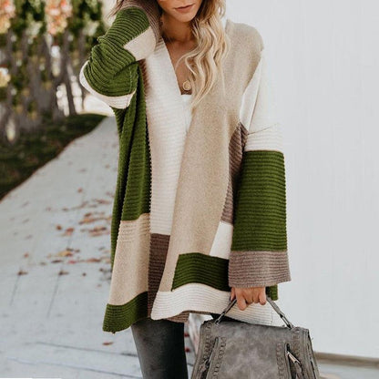 Frau in langem, gestreiftem Strickpullover in Grün, Beige und Weiß mit grauer Handtasche.