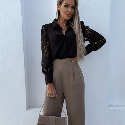Frau in schwarzer Spitzenbluse und beigen Hosen, hält eine beige Handtasche.