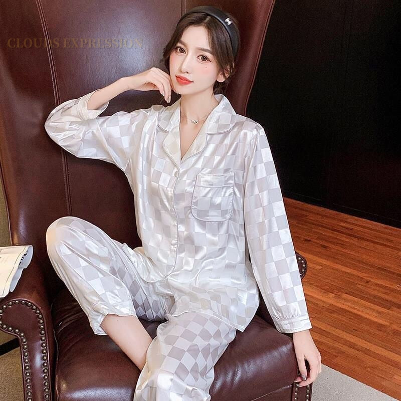 Frau in silbernem Satin-Pyjama mit Karomuster auf Ledersessel, Nachtwäsche, bequem, elegant.