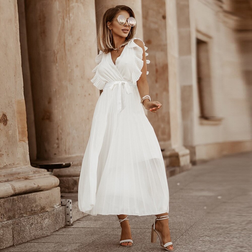 Frau in weißem Sommerkleid mit Rüschen, Sonnenbrille und High Heels vor historischer Architektur.