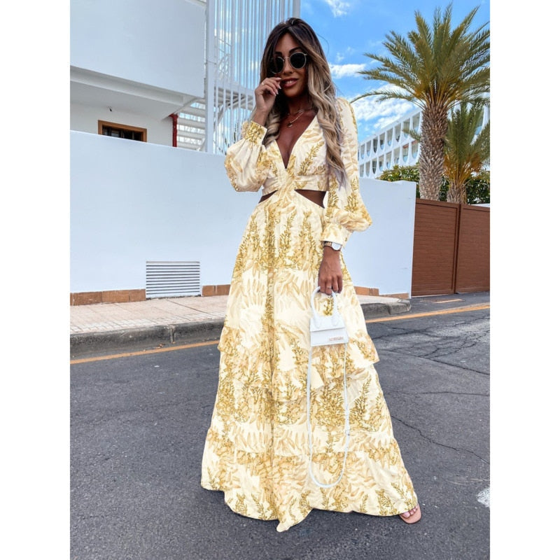 Frau in gelbem Maxikleid mit Blumenmuster, Sonnenbrille und weißer Handtasche auf der Straße.