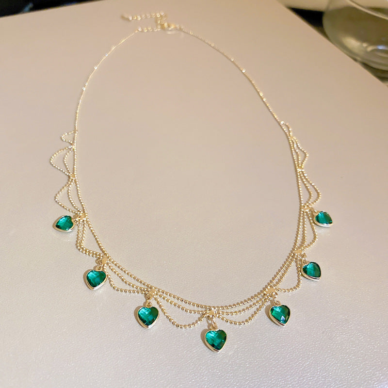 Goldene Halskette mit grünen Herzanhängern, elegantes Schmuckdesign, Damenaccessoire.