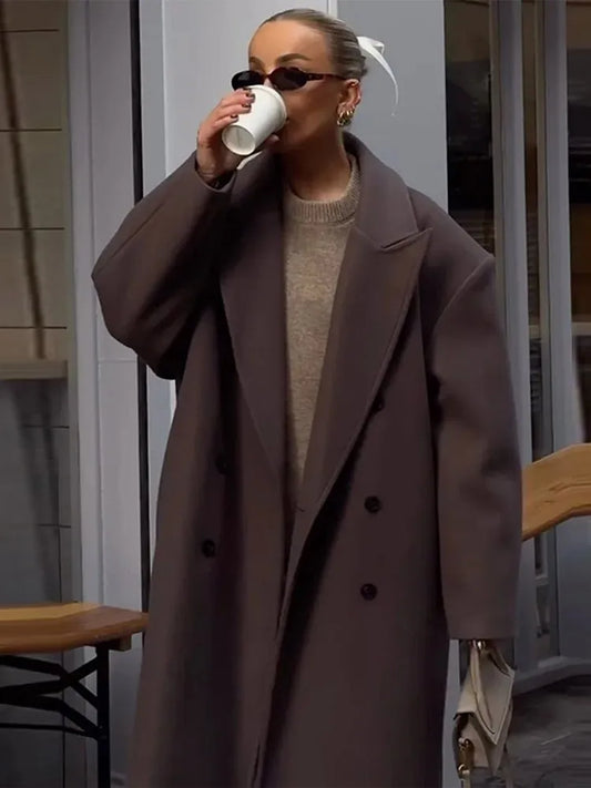Frau in braunem Wollmantel trinkt Kaffee, trägt Sonnenbrille, modisch, urbaner Stil.