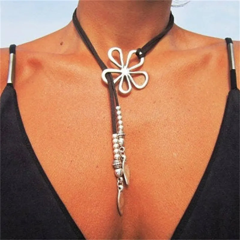 Frau mit schwarzem Lederhalsband, silbernem Kleeblatt-Anhänger und Perlen, eleganter Schmuck.