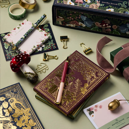 Luxus-Notizbuch mit goldener Prägung, Stifte, Briefpapier und Dekoration auf grünem Hintergrund.