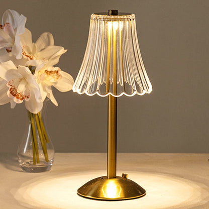 Goldene Tischlampe mit Glaslampenschirm, neben weißen Orchideen in Vase.