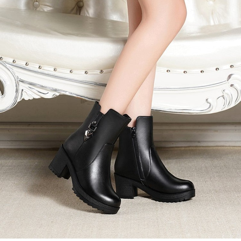 Schwarze Damenstiefeletten aus Leder mit Blockabsatz auf beigem Teppich.