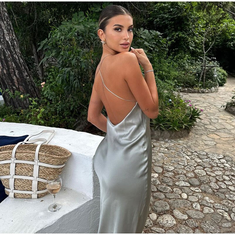 Frau im eleganten, silbernen Seidenkleid mit offenem Rücken, im Garten stehend.