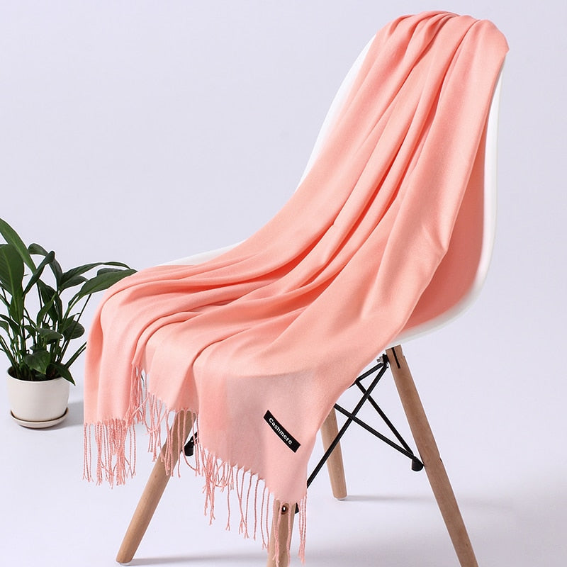 Rosa Kaschmirschal auf weißem Stuhl, weiche Fransen, elegantes Design, luxuriöses Accessoire.