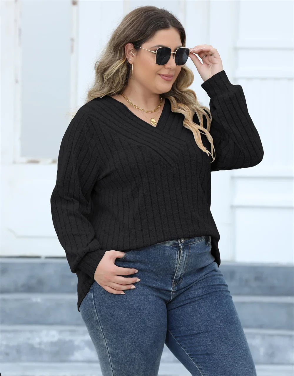 Frau in schwarzem Strickpullover und Jeans, trägt Sonnenbrille, lässiger Herbstlook.