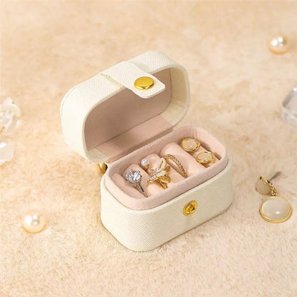 Beige Schmuckkästchen mit goldenen Ringen, Samtfutter, tragbar, elegant, Schmuckaufbewahrung.
