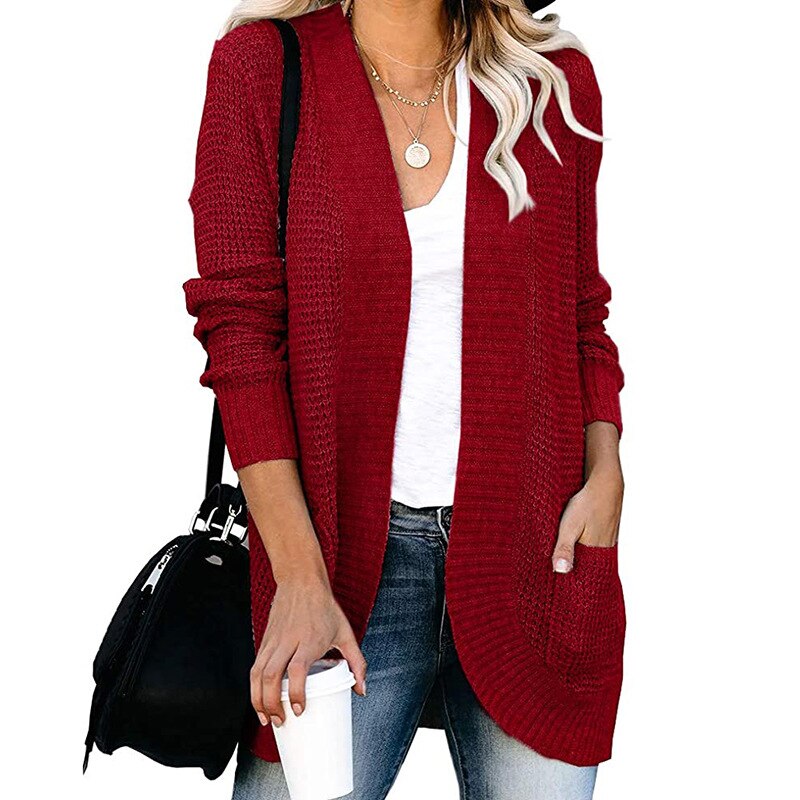 Frau in rotem Strickcardigan, weißem T-Shirt, Jeans, mit schwarzer Tasche und Kaffeebecher.