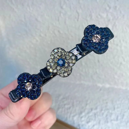 Närbild på en hårklämma med tre strassblommor i mörkblått och grått, med en blå sten i mitten, hållen i handen. 3