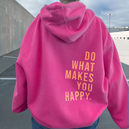 Frau in pinkem Hoodie mit gelbem Schriftzug "Do What Makes You Happy" im Freien.