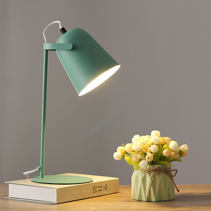 Grön bordslampa med tänd skärm på en bok, bredvid en ljusgrön kruka med blommor. 9