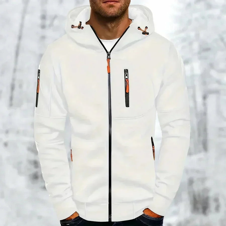 Man i vit huvtröja med dragkedja och orange dragkedjedetaljer, fotograferad framifrån mot en snöig skogsbakgrund. 3