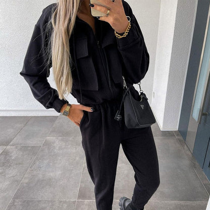 Frau in schwarzem Jogginganzug mit Tasche, lange blonde Haare, moderne Freizeitmode.
